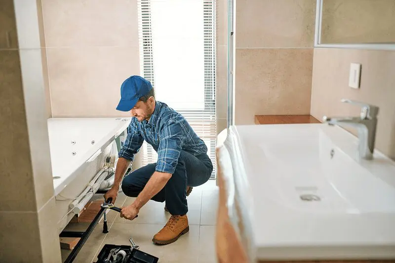 Plumber repairing bathtub in modern bathroom.