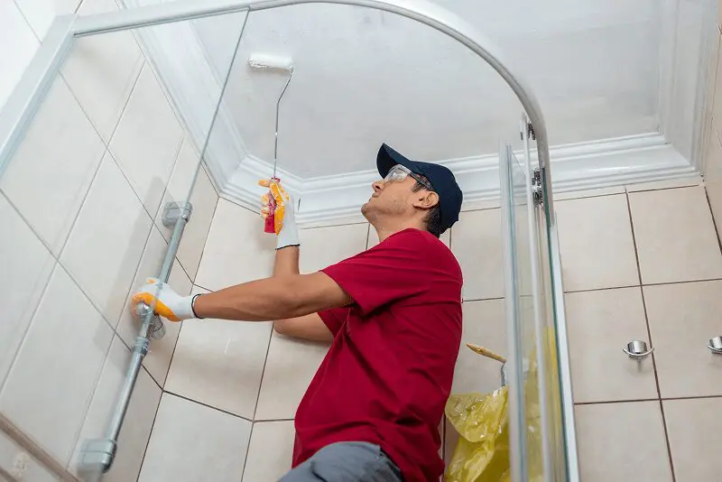 Person painting bathroom ceiling with roller brush.