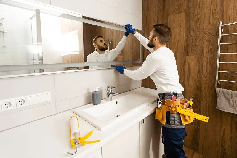 Man installing mirror in modern bathroom.