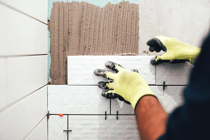 Person installing white tiles on wall.